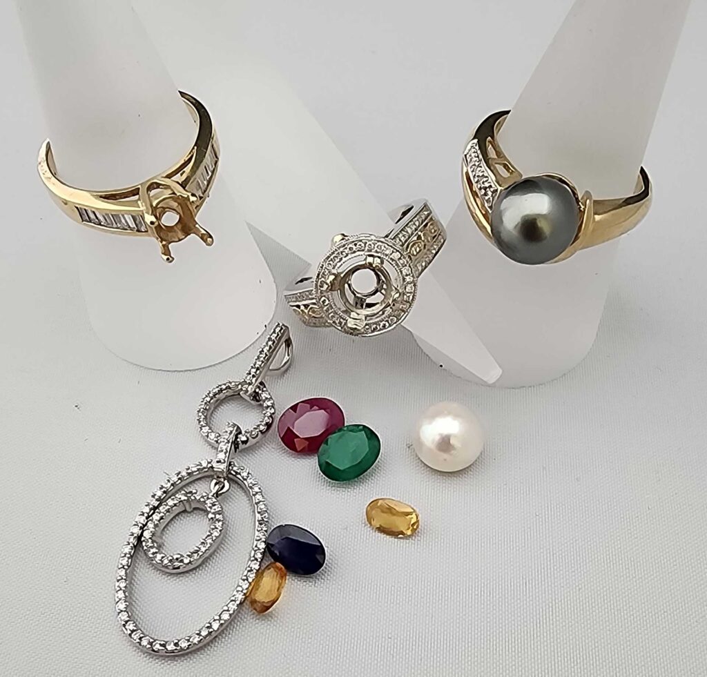 Custom jewelry design components including ring mountings, loose gemstones, and diamond pendant.