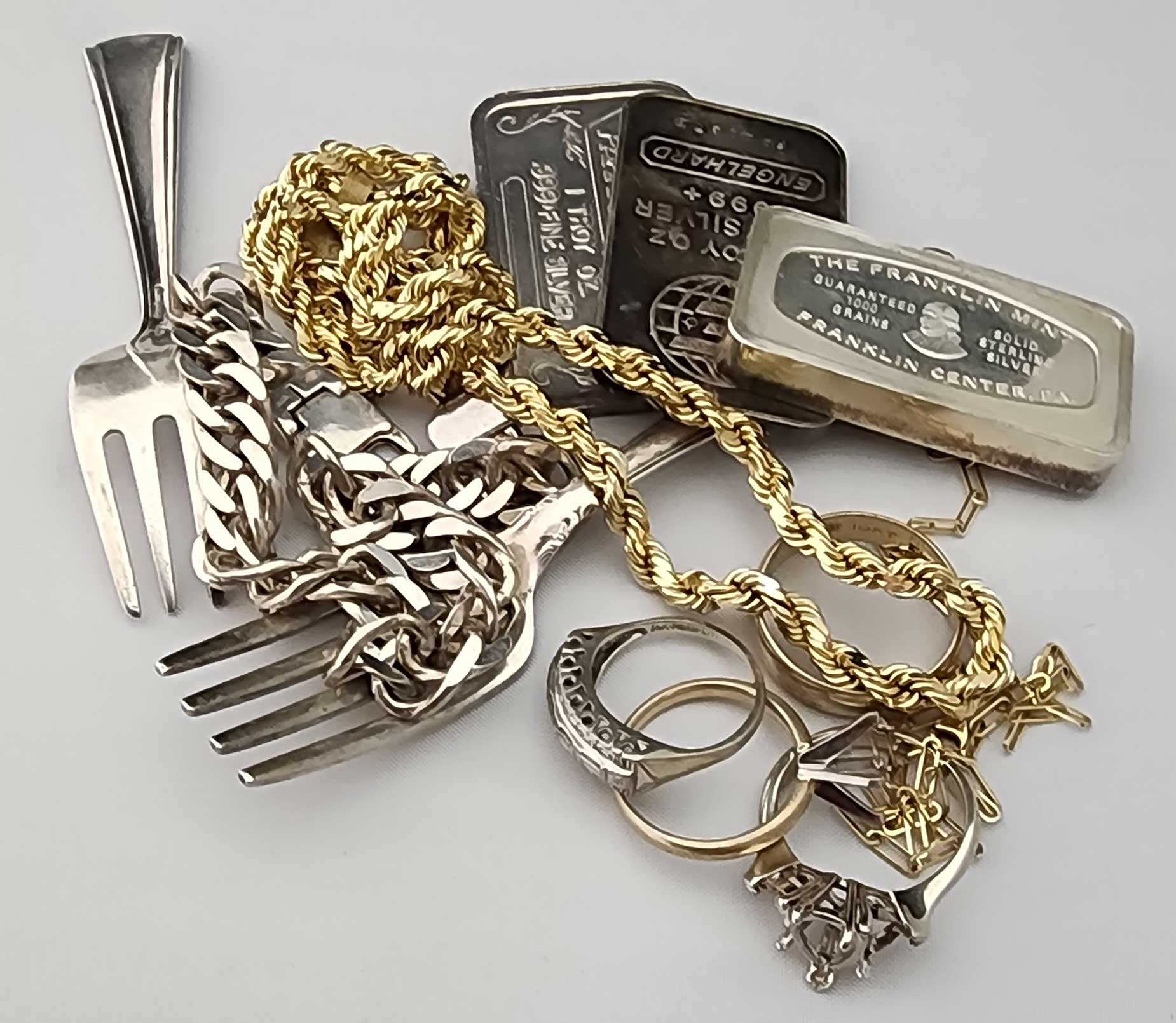 Assortment of gold and silver jewelry, chains, rings, and bullion bars on a white background.