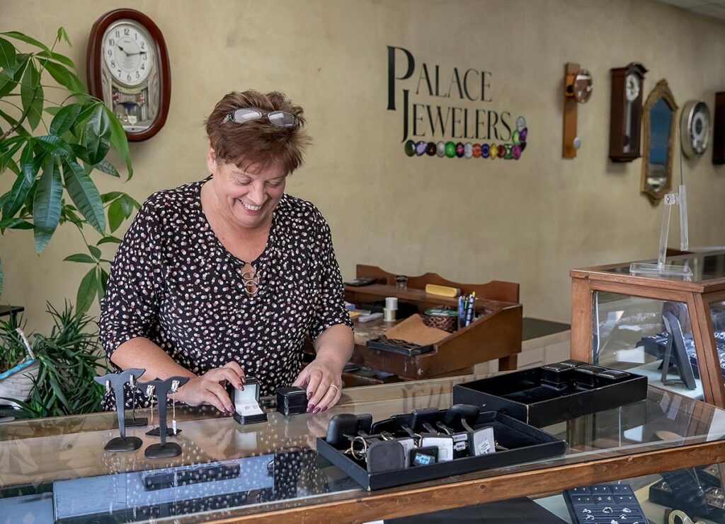 Owner of Palace Jewelers smiling while arranging jewelry in a display case.