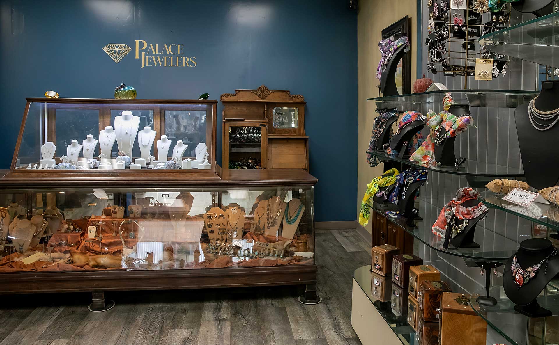 Palace Jewelers display case of necklaces with a blue accent wall and shelves of scarves and jewelry to the side.