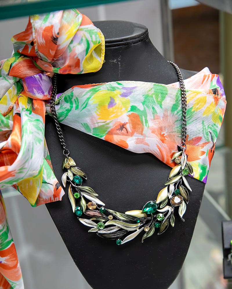 Leaf-inspired necklace with green gemstones styled with a bright floral scarf on a display bust.